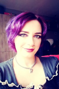 A woman with purple hair, representing The Plural Association, is posing for a picture to raise awareness about OSDD and promote the Power to the Plurals.